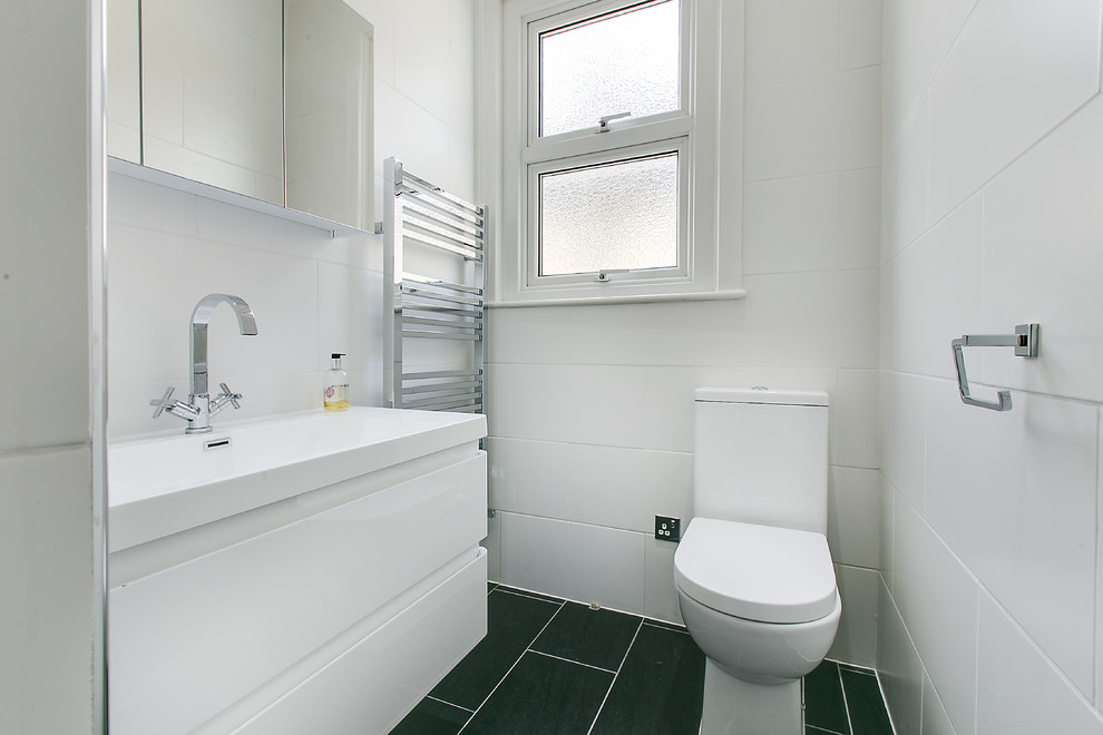 This is an example of a small transitional 3/4 bathroom in London with a drop-in sink, furniture-like cabinets, white cabinets, solid surface benchtops, a curbless shower, a one-piece toilet, white tile, ceramic tile, white walls and ceramic floors.