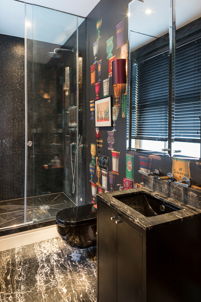 This is an example of a mid-sized eclectic bathroom in London with flat-panel cabinets, black cabinets, an open shower, a wall-mount toilet, black walls, marble floors, marble benchtops, black floor, a sliding shower screen and black benchtops.
