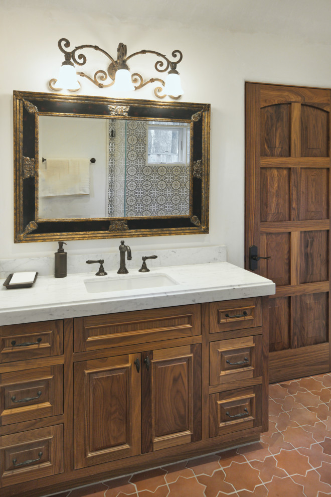 This is an example of a medium sized mediterranean bathroom in San Francisco with raised-panel cabinets, medium wood cabinets, white walls, porcelain flooring, a submerged sink, marble worktops, red floors, white worktops, a single sink and a built in vanity unit.