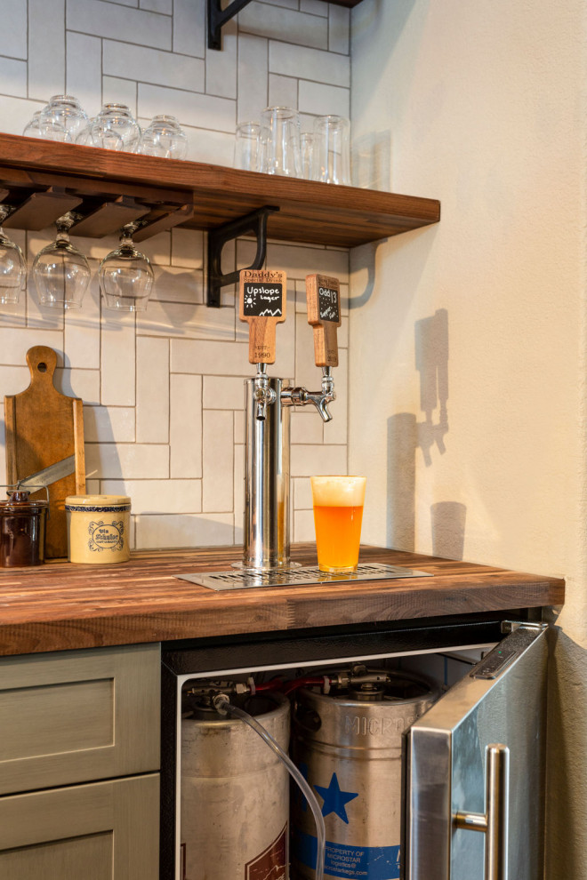 Example of a mid-sized farmhouse single-wall medium tone wood floor and brown floor wet bar design in Denver with an undermount sink, shaker cabinets, distressed cabinets, wood countertops, white backsplash, ceramic backsplash and brown countertops