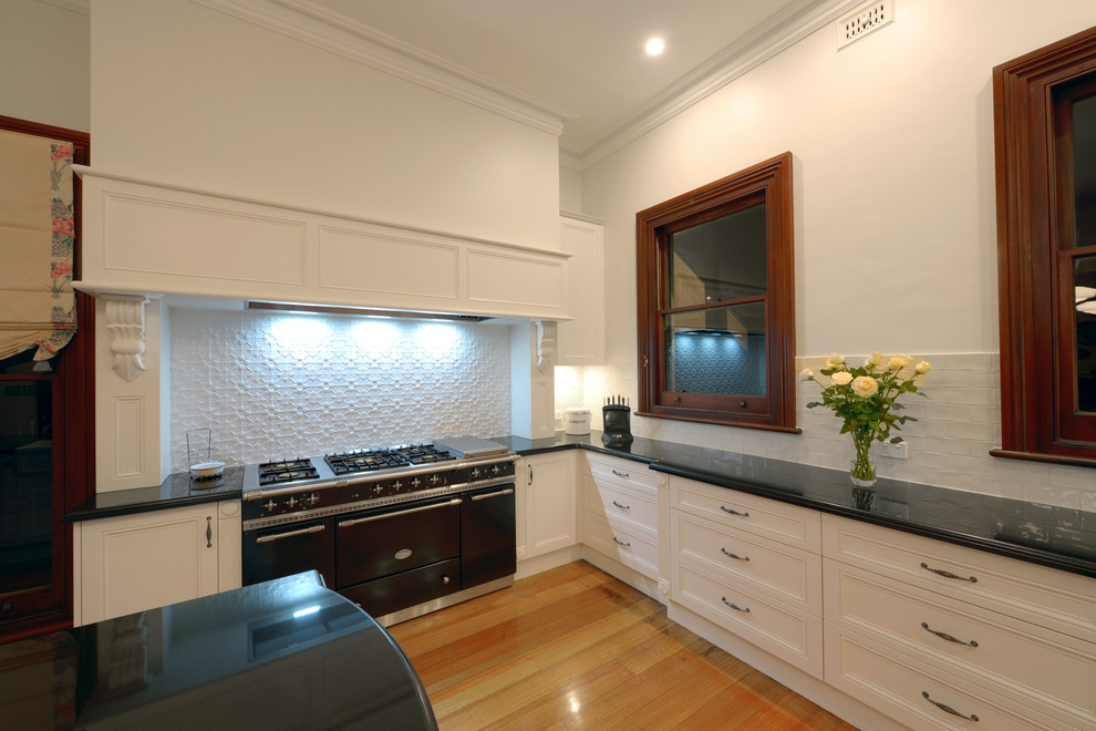 Inspiration for an expansive traditional u-shaped eat-in kitchen in Newcastle - Maitland with a farmhouse sink, recessed-panel cabinets, white cabinets, granite benchtops, white splashback, subway tile splashback, medium hardwood floors and with island.