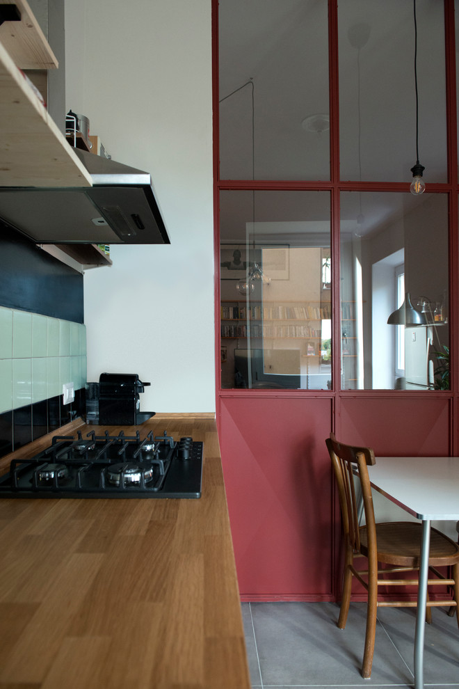 Small contemporary single-wall eat-in kitchen in Rome with an integrated sink, flat-panel cabinets, black cabinets, wood benchtops, black splashback, ceramic splashback, black appliances, porcelain floors, no island and grey floor.