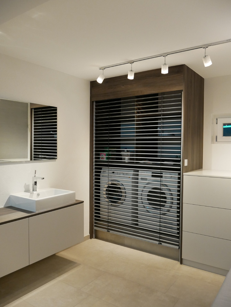 Hauswirtschaftsraum in L-Form With Waschbecken, flächenbündigen Schrankfronten, beigen Schränken, weißer Wandfarbe, Waschmaschine und Trockner versteckt, beigem Boden and beiger Arbeitsplatte in Frankfurt