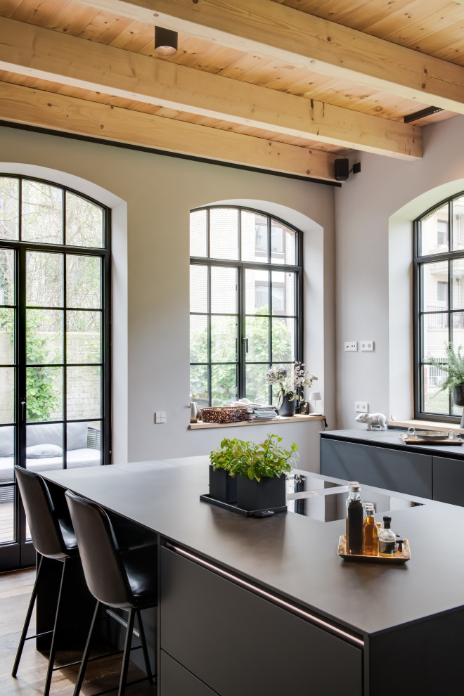 Inspiration for a large contemporary galley open plan kitchen in Hamburg with a single-bowl sink, flat-panel cabinets, grey cabinets, quartz benchtops, stainless steel appliances, medium hardwood floors, with island, brown floor, grey benchtop and exposed beam.