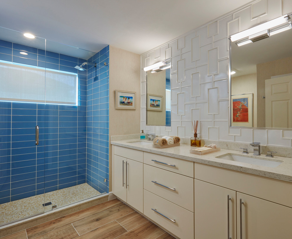 This is an example of a beach style 3/4 bathroom in Miami with flat-panel cabinets, beige cabinets, an alcove shower, blue tile, glass tile, an undermount sink, a hinged shower door and beige floor.