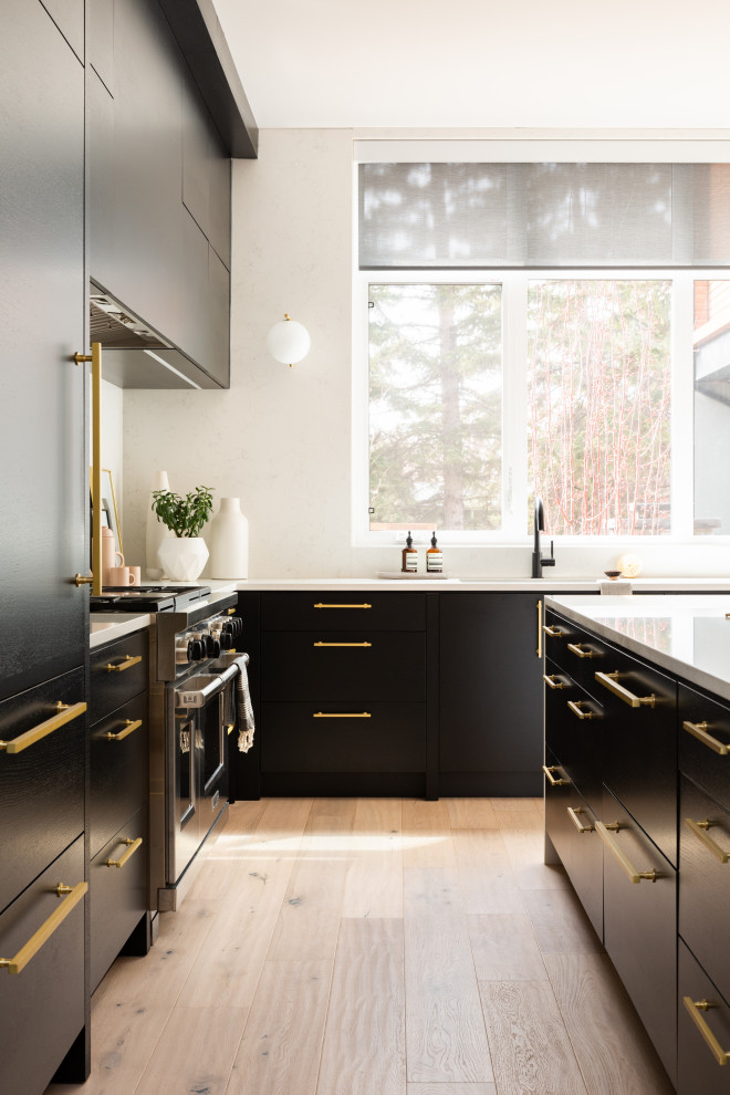 Large contemporary l-shaped eat-in kitchen in Calgary with an undermount sink, flat-panel cabinets, black cabinets, quartzite benchtops, white splashback, engineered quartz splashback, stainless steel appliances, light hardwood floors, with island, brown floor and white benchtop.