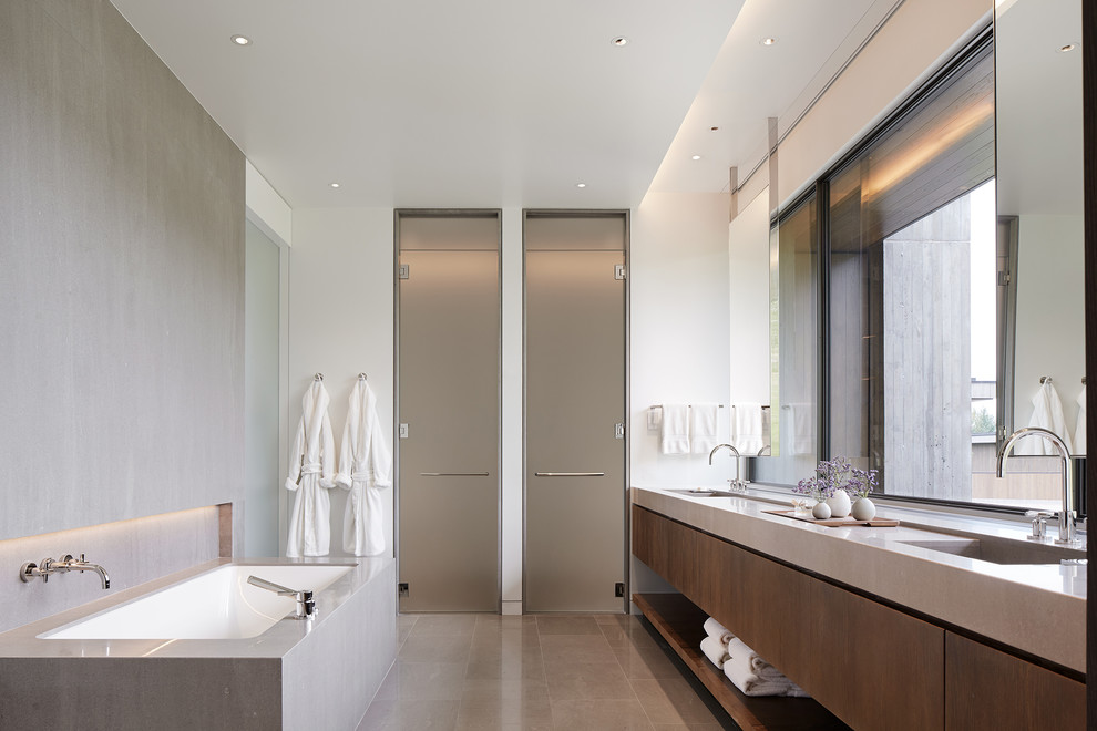 This is an example of a modern bathroom in Denver with flat-panel cabinets, white tile, white walls, limestone floors, an integrated sink, limestone benchtops, grey floor, dark wood cabinets, an undermount tub and a curbless shower.