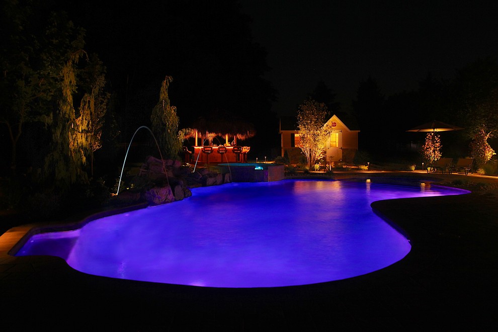 This is an example of a mid-sized traditional backyard custom-shaped pool in Philadelphia with a pool house and concrete pavers.