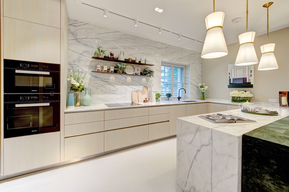 This is an example of a contemporary u-shaped eat-in kitchen in London with an undermount sink, flat-panel cabinets, beige cabinets, white splashback, stone slab splashback, black appliances, a peninsula and white floor.