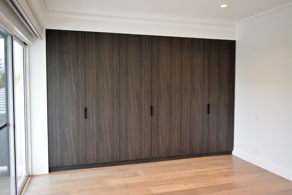 This is an example of a large modern gender-neutral built-in wardrobe in Sydney with flat-panel cabinets and dark wood cabinets.