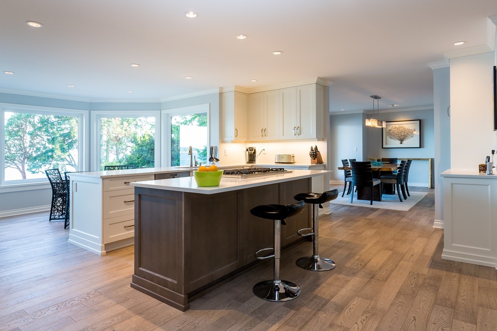 This is an example of a large contemporary l-shaped eat-in kitchen in Other with recessed-panel cabinets, white cabinets, stainless steel appliances, medium hardwood floors, with island, quartz benchtops and white benchtop.