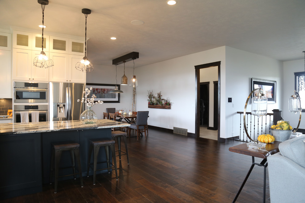 Mid-sized transitional l-shaped dark wood floor eat-in kitchen photo with a farmhouse sink, recessed-panel cabinets, white cabinets, granite countertops, black backsplash, porcelain backsplash, stainless steel appliances and an island