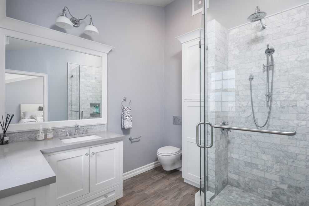 Mid-sized transitional master bathroom in Los Angeles with beaded inset cabinets, white cabinets, a corner shower, a wall-mount toilet, gray tile, porcelain tile, grey walls, ceramic floors, an undermount sink, engineered quartz benchtops, brown floor, a hinged shower door and grey benchtops.