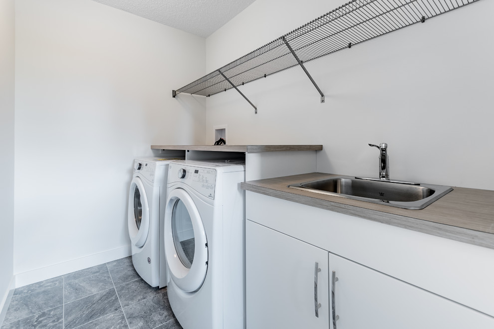 Inspiration for a mid-sized contemporary galley dedicated laundry room in Edmonton with a drop-in sink, flat-panel cabinets, white cabinets, laminate benchtops, white walls, ceramic floors, a side-by-side washer and dryer and grey floor.