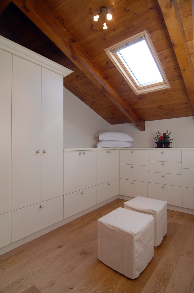 Photo of a contemporary walk-in wardrobe in Other with white cabinets and light hardwood floors.