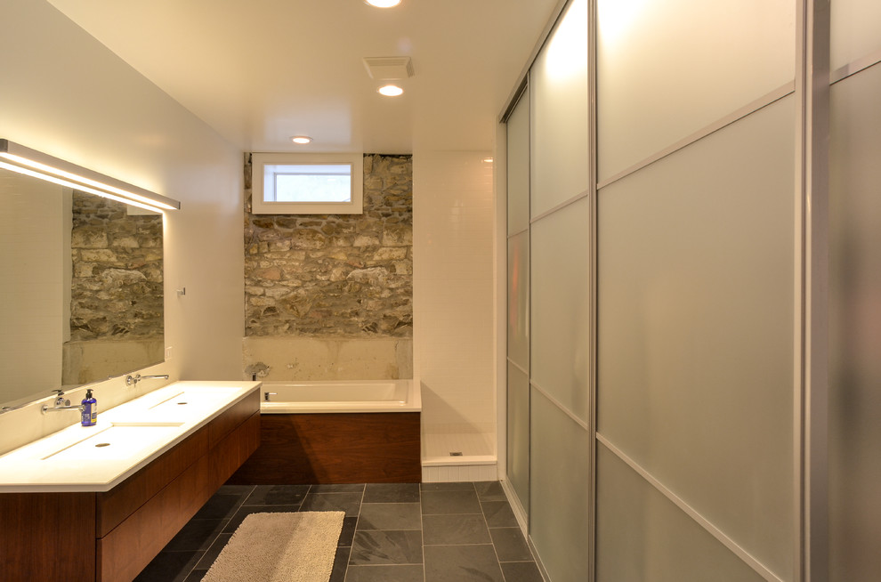 This is an example of a mid-sized contemporary master bathroom in Denver with flat-panel cabinets, medium wood cabinets, a drop-in tub, a corner shower, gray tile, stone tile, white walls, slate floors, an integrated sink, solid surface benchtops, grey floor and an open shower.