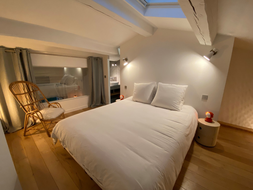 This is an example of a large bedroom in Other with light hardwood flooring and exposed beams.