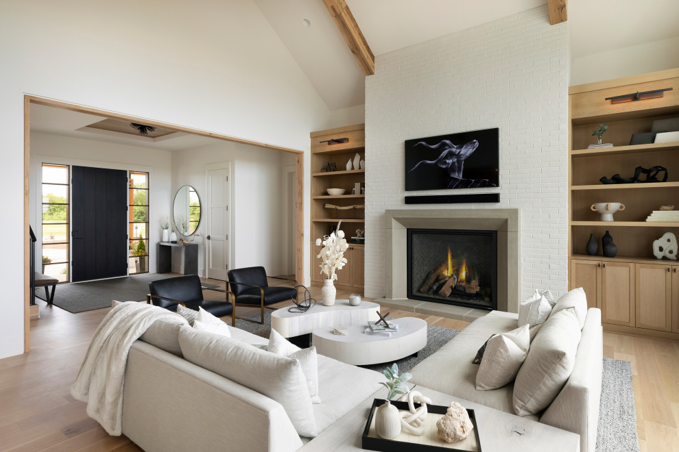Modelo de salón abierto y abovedado clásico renovado con paredes blancas, suelo de madera clara, todas las chimeneas, marco de chimenea de piedra y televisor colgado en la pared