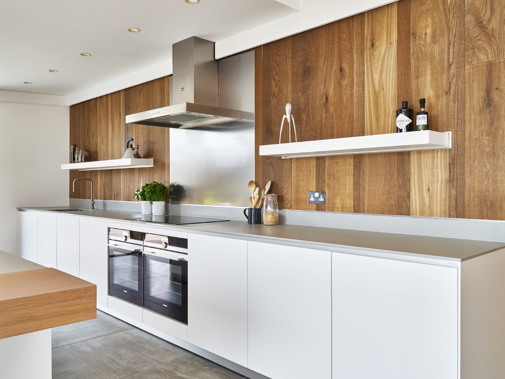 Design ideas for a large country galley open plan kitchen in Devon with flat-panel cabinets, with island, an integrated sink, white cabinets, solid surface benchtops, metallic splashback, metal splashback, black appliances, ceramic floors, grey floor and grey benchtop.