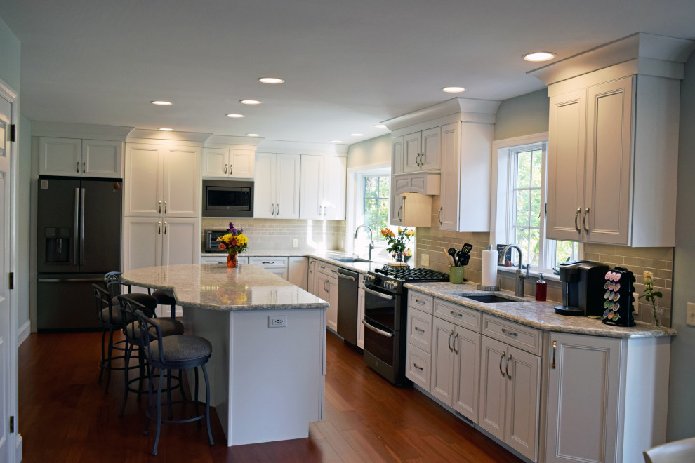 Transitional medium tone wood floor kitchen photo with an undermount sink, recessed-panel cabinets, white cabinets, quartz countertops, gray backsplash, subway tile backsplash, stainless steel appliances and an island