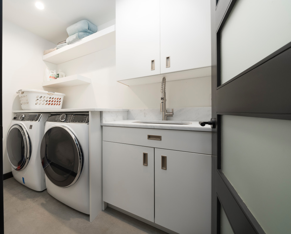 Foto på en mellanstor industriell parallell tvättstuga enbart för tvätt, med släta luckor, vita skåp och en tvättmaskin och torktumlare bredvid varandra