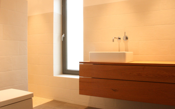 Immagine di una stanza da bagno con doccia moderna di medie dimensioni con ante lisce, ante in legno bruno, vasca ad alcova, doccia alcova, WC sospeso, piastrelle beige, piastrelle di vetro, pareti bianche, pavimento in bambù, lavabo a bacinella e top in legno