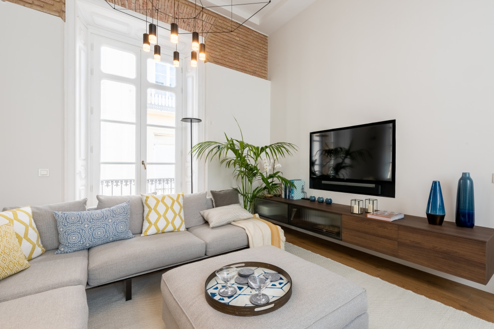 Esempio di un soggiorno minimal aperto con pareti bianche, pavimento in legno massello medio, TV a parete, libreria, pavimento marrone e pareti in mattoni