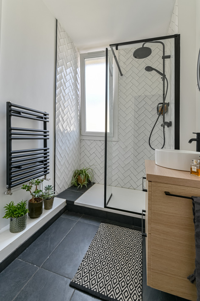 Skandinavisk inredning av ett litet badrum med dusch, med luckor med profilerade fronter, skåp i ljust trä, en kantlös dusch, en vägghängd toalettstol, vit kakel, perrakottakakel, vita väggar, klinkergolv i terrakotta, ett väggmonterat handfat och grått golv