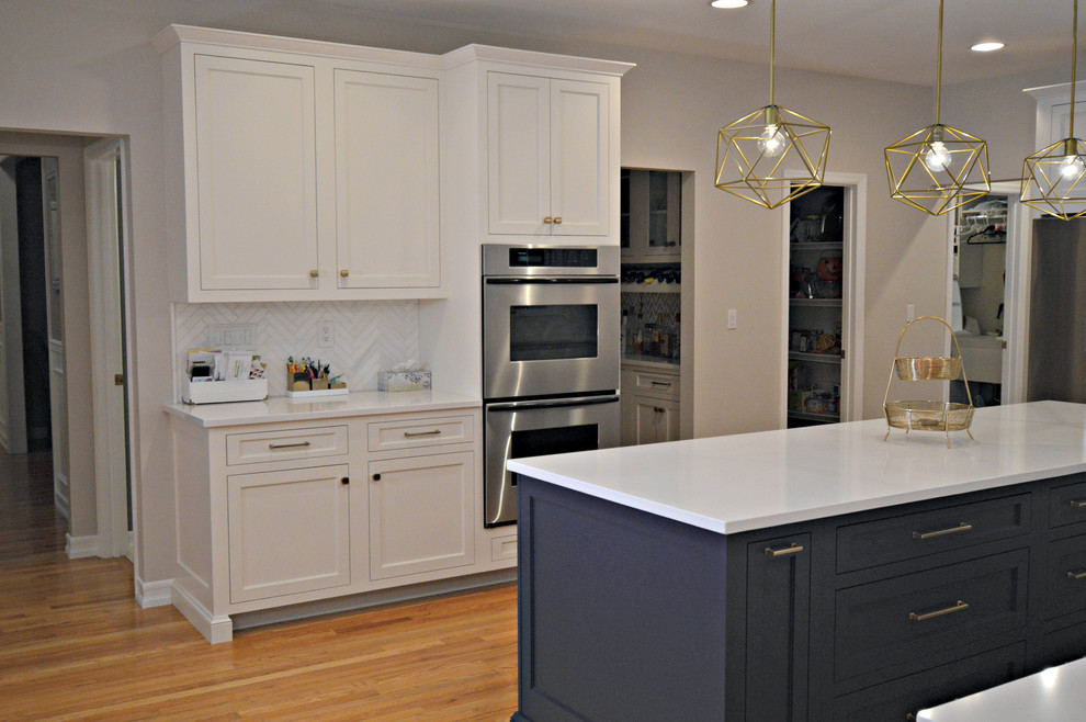 This is an example of a large transitional l-shaped open plan kitchen in New York with an undermount sink, recessed-panel cabinets, white cabinets, quartzite benchtops, white splashback, marble splashback, stainless steel appliances, medium hardwood floors, with island, brown floor and white benchtop.