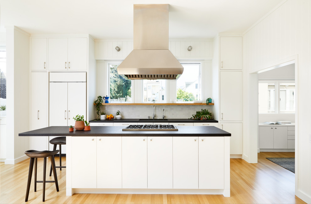 Inspiration for a large contemporary galley open plan kitchen in San Francisco with an undermount sink, flat-panel cabinets, white cabinets, panelled appliances, light hardwood floors, with island, black benchtop, white splashback and beige floor.
