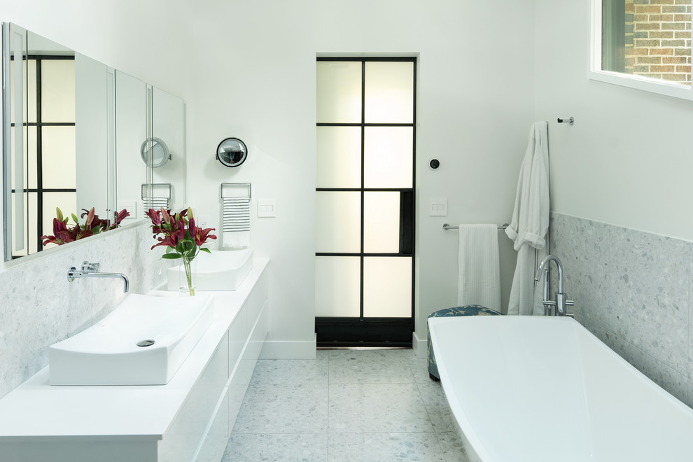 This is an example of a contemporary master bathroom in Denver with flat-panel cabinets, white cabinets, a freestanding tub, a curbless shower, a one-piece toilet, white tile, marble, white walls, terrazzo floors, a vessel sink, engineered quartz benchtops, white floor, a sliding shower screen and white benchtops.