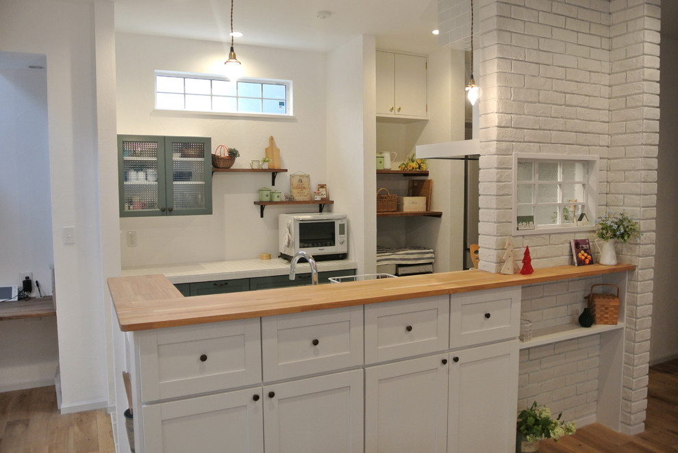 Design ideas for a mid-sized country single-wall eat-in kitchen in Nagoya with flat-panel cabinets, white cabinets, a peninsula, white splashback, subway tile splashback, stainless steel appliances, an undermount sink, terra-cotta floors and wood benchtops.