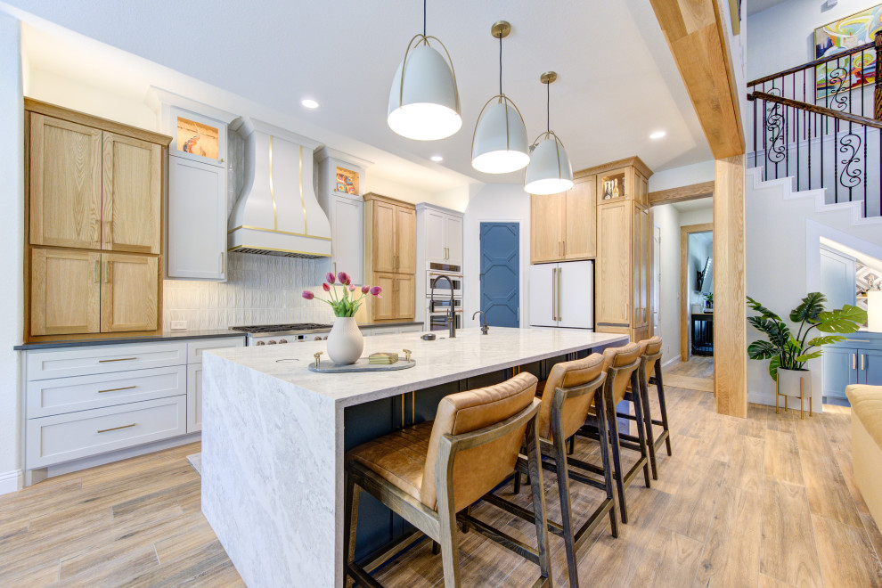 Transitional l-shaped medium tone wood floor and brown floor kitchen photo in Houston with shaker cabinets, light wood cabinets, white backsplash, white appliances, an island and gray countertops