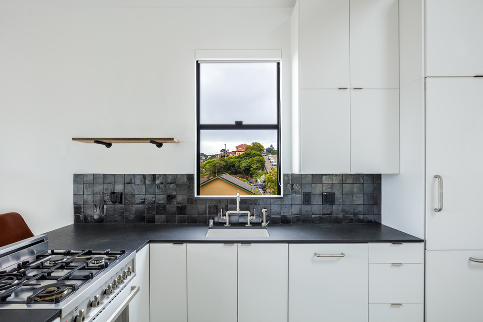 Photo of a mid-sized scandinavian l-shaped open plan kitchen in San Francisco with an undermount sink, flat-panel cabinets, black benchtop, solid surface benchtops, grey splashback, light hardwood floors, no island and brown floor.