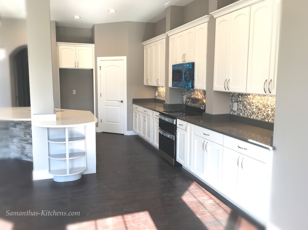 Home design - mid-sized transitional l-shaped dark wood floor home design idea with an undermount sink, recessed-panel cabinets, white cabinets, quartz countertops, gray backsplash, ceramic backsplash, stainless steel appliances and an island
