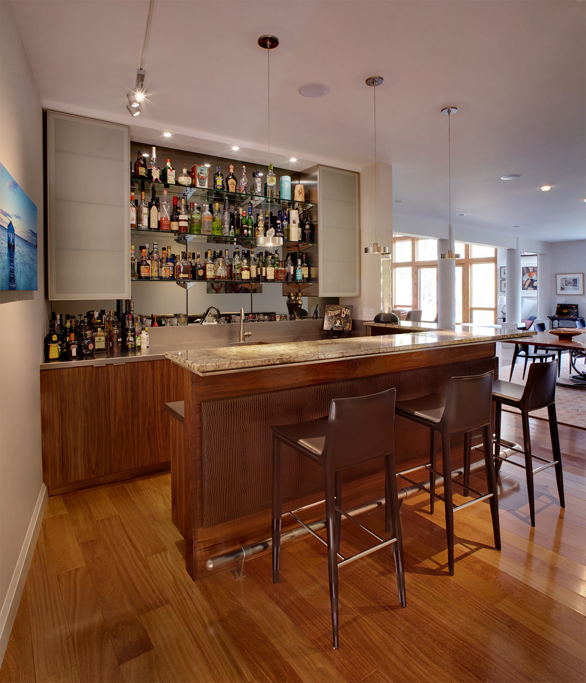 Inspiration for a contemporary u-shaped seated home bar in New York with medium hardwood floors, flat-panel cabinets, dark wood cabinets, mirror splashback and brown floor.