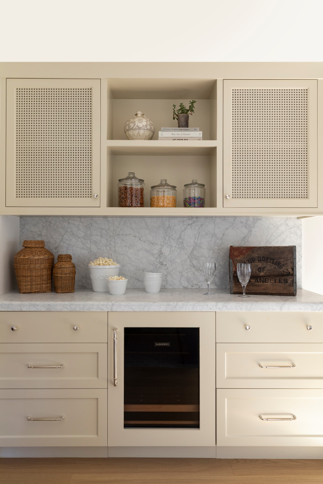 Example of a beach style medium tone wood floor home bar design in Orange County with white backsplash, stone slab backsplash and white countertops