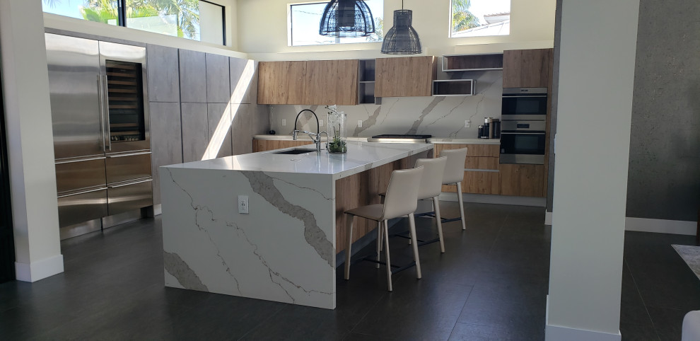 Large contemporary eat-in kitchen in Miami with an undermount sink, flat-panel cabinets, grey cabinets, quartz benchtops, white splashback, engineered quartz splashback, stainless steel appliances, with island, black floor and white benchtop.