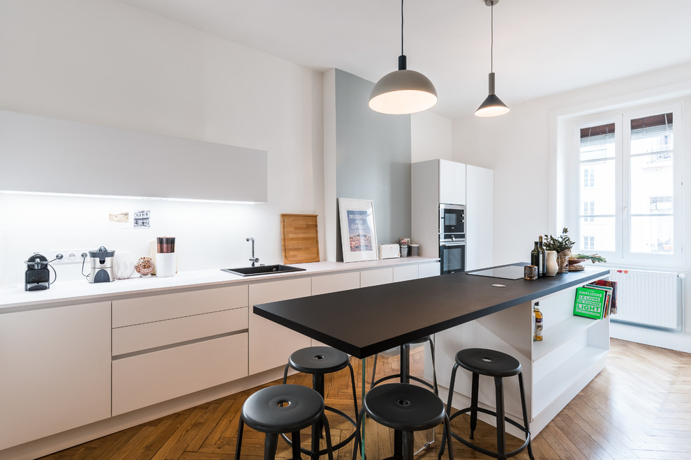 This is an example of a large contemporary kitchen in Lyon with laminate benchtops, stainless steel appliances, with island, a drop-in sink, flat-panel cabinets, white splashback, medium hardwood floors and orange floor.