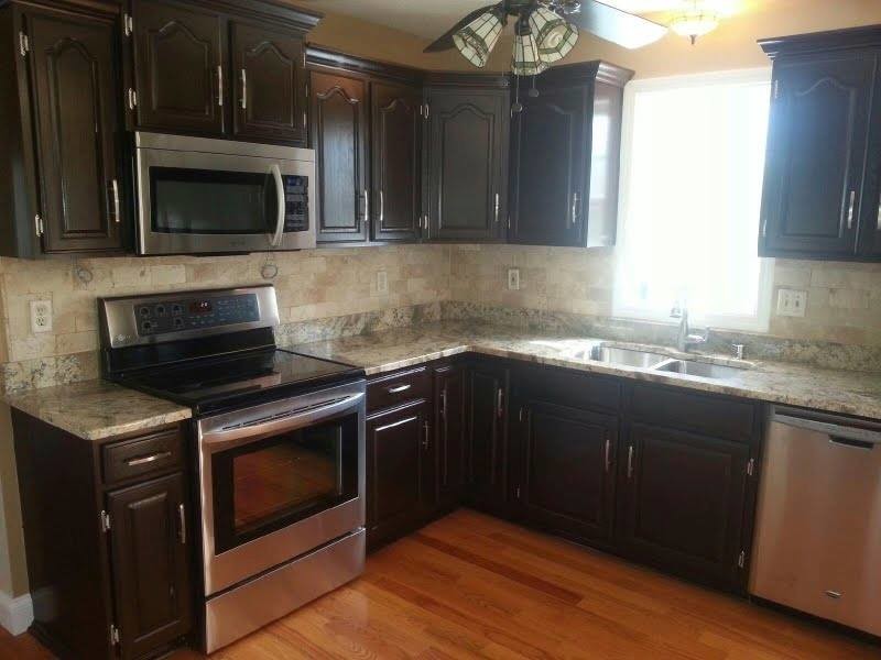 Example of a l-shaped medium tone wood floor open concept kitchen design with a double-bowl sink, raised-panel cabinets, dark wood cabinets, granite countertops, multicolored backsplash, ceramic backsplash and stainless steel appliances