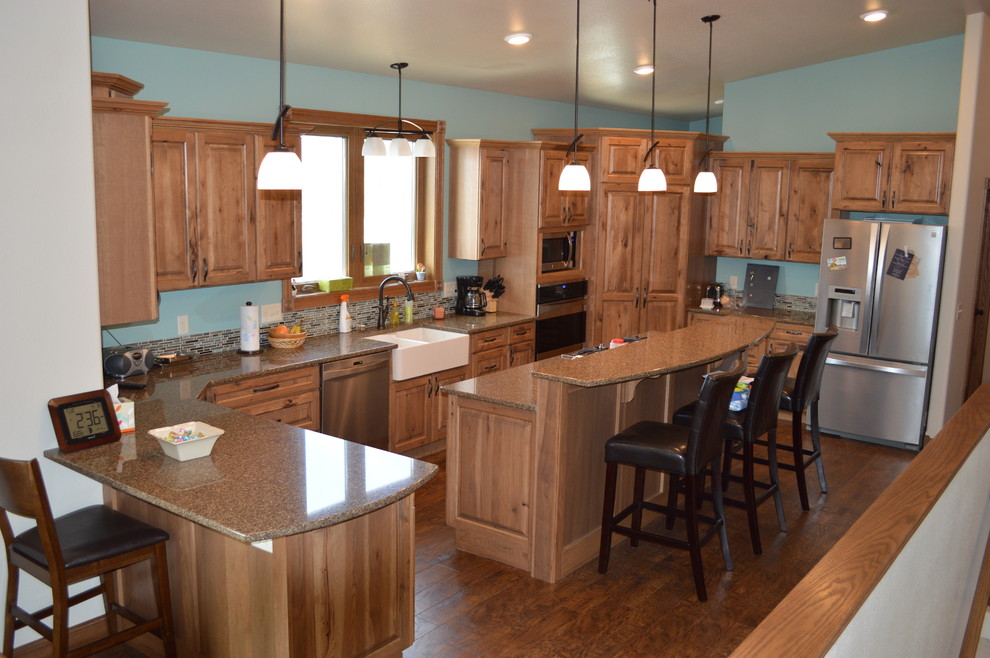 This is an example of a country u-shaped kitchen in Other with a farmhouse sink, raised-panel cabinets, light wood cabinets, quartzite benchtops, stainless steel appliances, vinyl floors and with island.