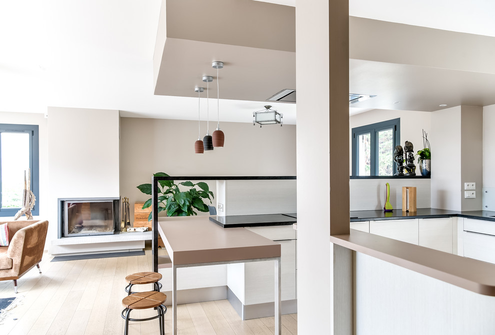 Photo of a large modern l-shaped eat-in kitchen in Lyon with an undermount sink, flat-panel cabinets, medium wood cabinets, granite benchtops, orange splashback, stainless steel appliances, light hardwood floors, a peninsula, timber splashback, beige floor and grey benchtop.