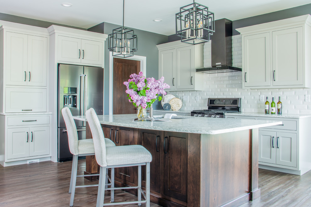 Inspiration for a transitional l-shaped brown floor open concept kitchen remodel with an undermount sink, white cabinets, white backsplash, stainless steel appliances, an island, white countertops and shaker cabinets