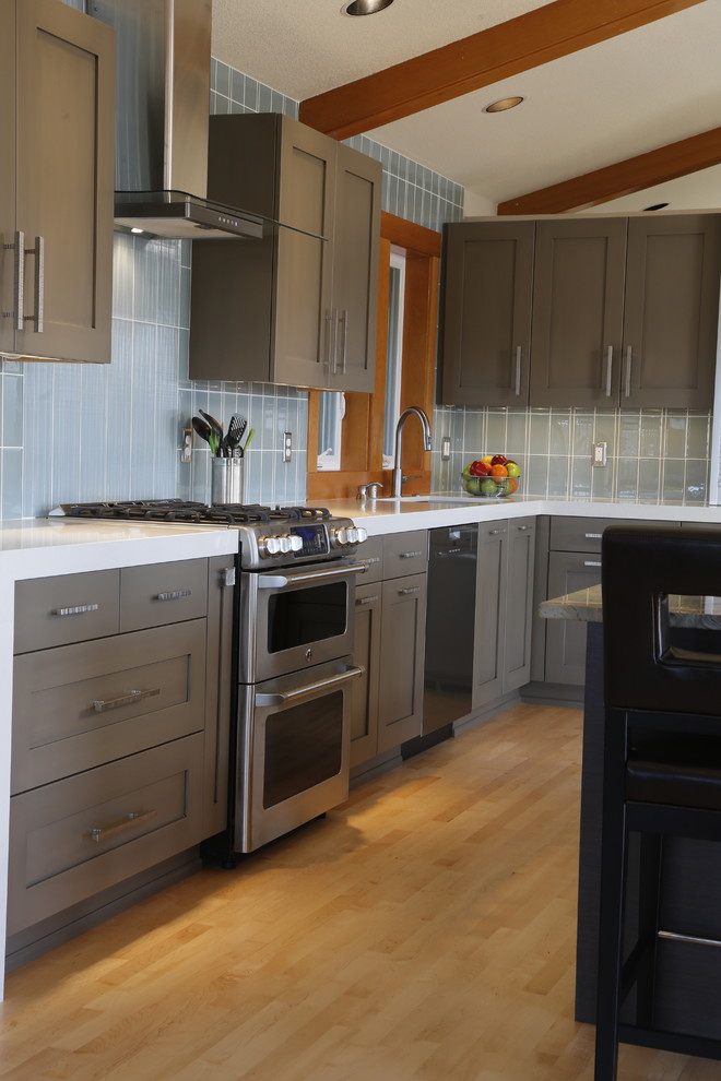 This is an example of a mid-sized transitional l-shaped open plan kitchen in Seattle with an undermount sink, recessed-panel cabinets, grey cabinets, quartz benchtops, blue splashback, ceramic splashback, stainless steel appliances, light hardwood floors and with island.