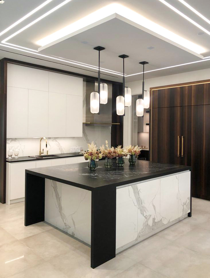This is an example of a large modern u-shaped eat-in kitchen in New York with an undermount sink, flat-panel cabinets, white cabinets, marble benchtops, white splashback, marble splashback, black appliances, porcelain floors, with island, beige floor, black benchtop and recessed.