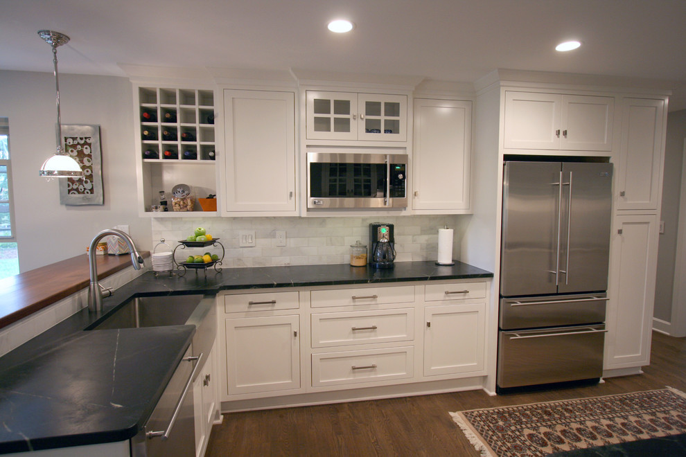 Inspiration for a mid-sized l-shaped dark wood floor kitchen remodel in Cincinnati with a farmhouse sink, flat-panel cabinets, white cabinets, soapstone countertops, white backsplash, stone tile backsplash, stainless steel appliances and a peninsula