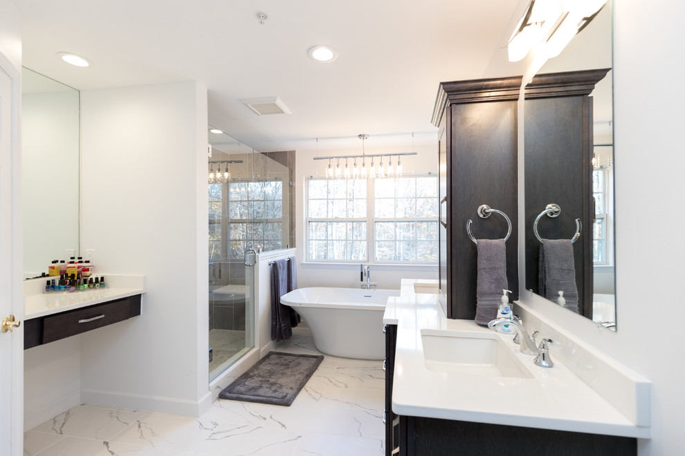 This is an example of a mid-sized contemporary master bathroom in DC Metro with a freestanding tub, white walls, an undermount sink, a hinged shower door, engineered quartz benchtops, shaker cabinets, dark wood cabinets, an alcove shower, a two-piece toilet, gray tile, porcelain tile and marble floors.