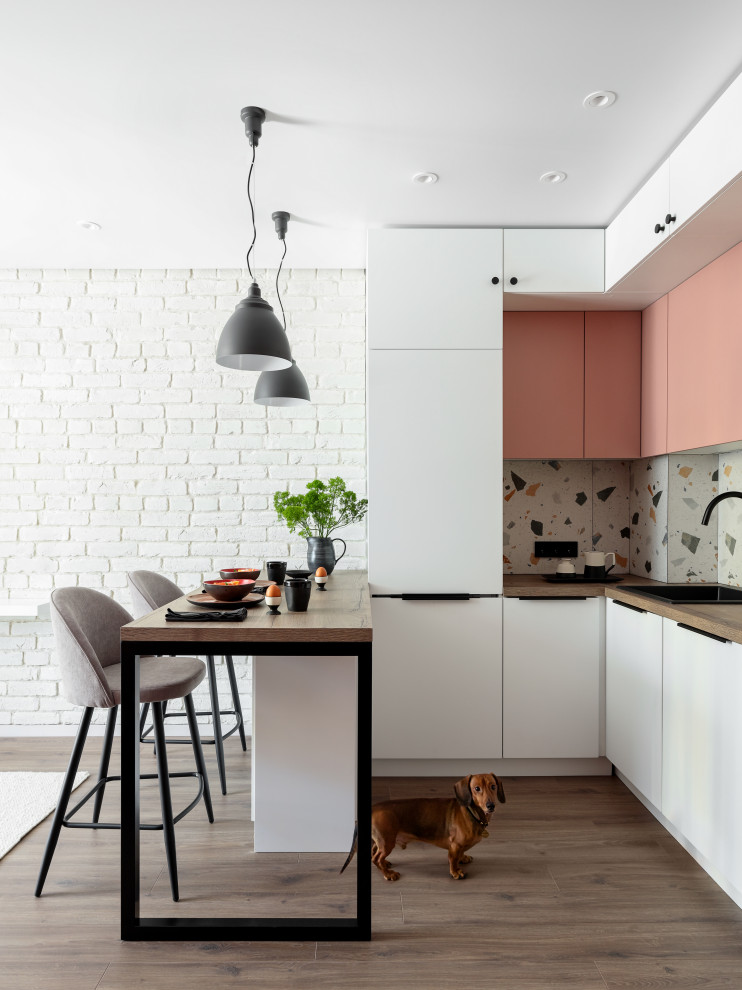 Small scandinavian l-shaped eat-in kitchen in Saint Petersburg with a single-bowl sink, flat-panel cabinets, pink cabinets, wood benchtops, multi-coloured splashback, porcelain splashback, stainless steel appliances, medium hardwood floors, brown floor and brown benchtop.