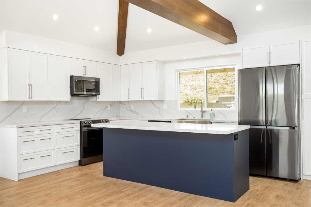 Inspiration for a medium sized classic l-shaped open plan kitchen in Los Angeles with a belfast sink, shaker cabinets, blue cabinets, engineered stone countertops, white splashback, engineered quartz splashback, stainless steel appliances, laminate floors, an island, brown floors, white worktops and exposed beams.