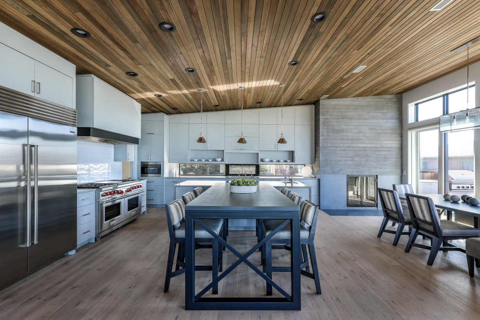Trendy u-shaped medium tone wood floor, brown floor, vaulted ceiling and wood ceiling eat-in kitchen photo in Portland with an undermount sink, flat-panel cabinets, white cabinets, white backsplash, window backsplash, stainless steel appliances, an island and gray countertops